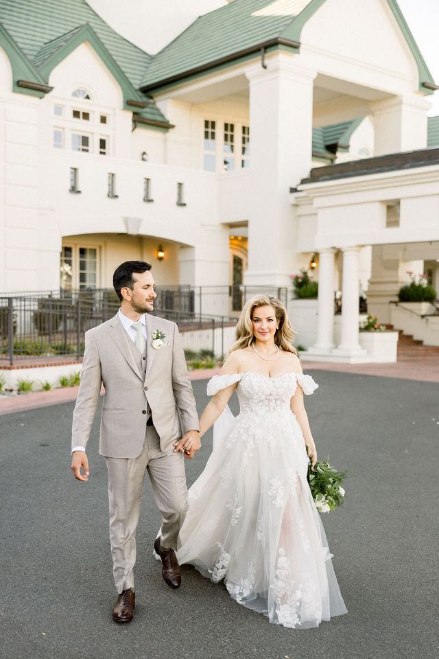 Britt and Chris walk hand in hand in front of the clubhouse