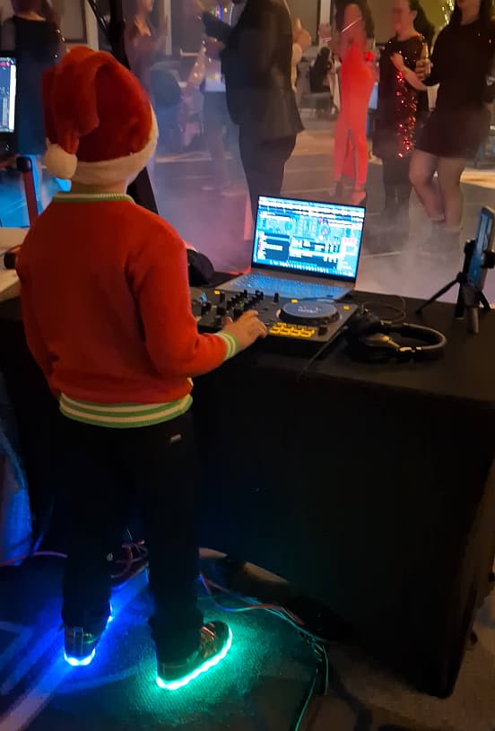 A young DJ student in a Santa hat mixing at a holiday party