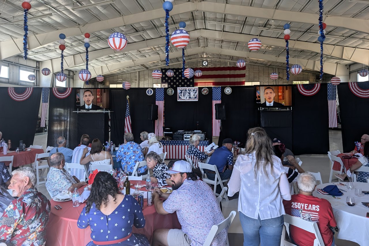 Guests at red, white and blue tables facing the USO stage in a decorated hangar