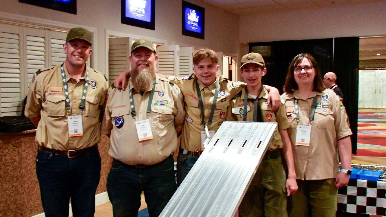 A group in scout uniforms holding a section of the derby race track