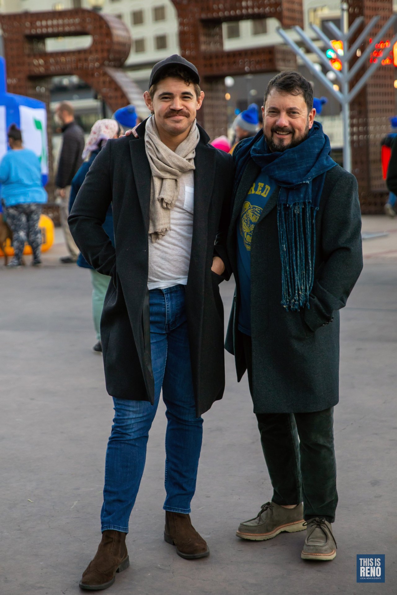 Two friends smile in front of the City Plaza menorah