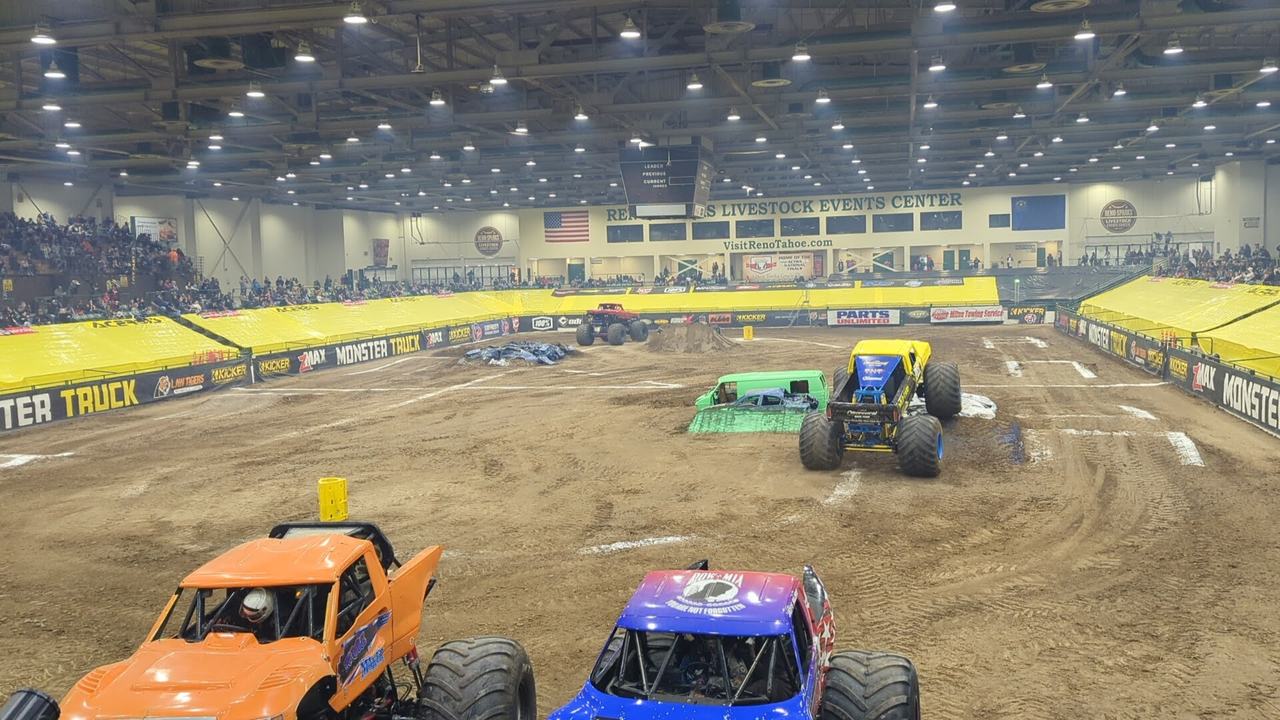 An orange and a blue monster truck parked side by side on the track