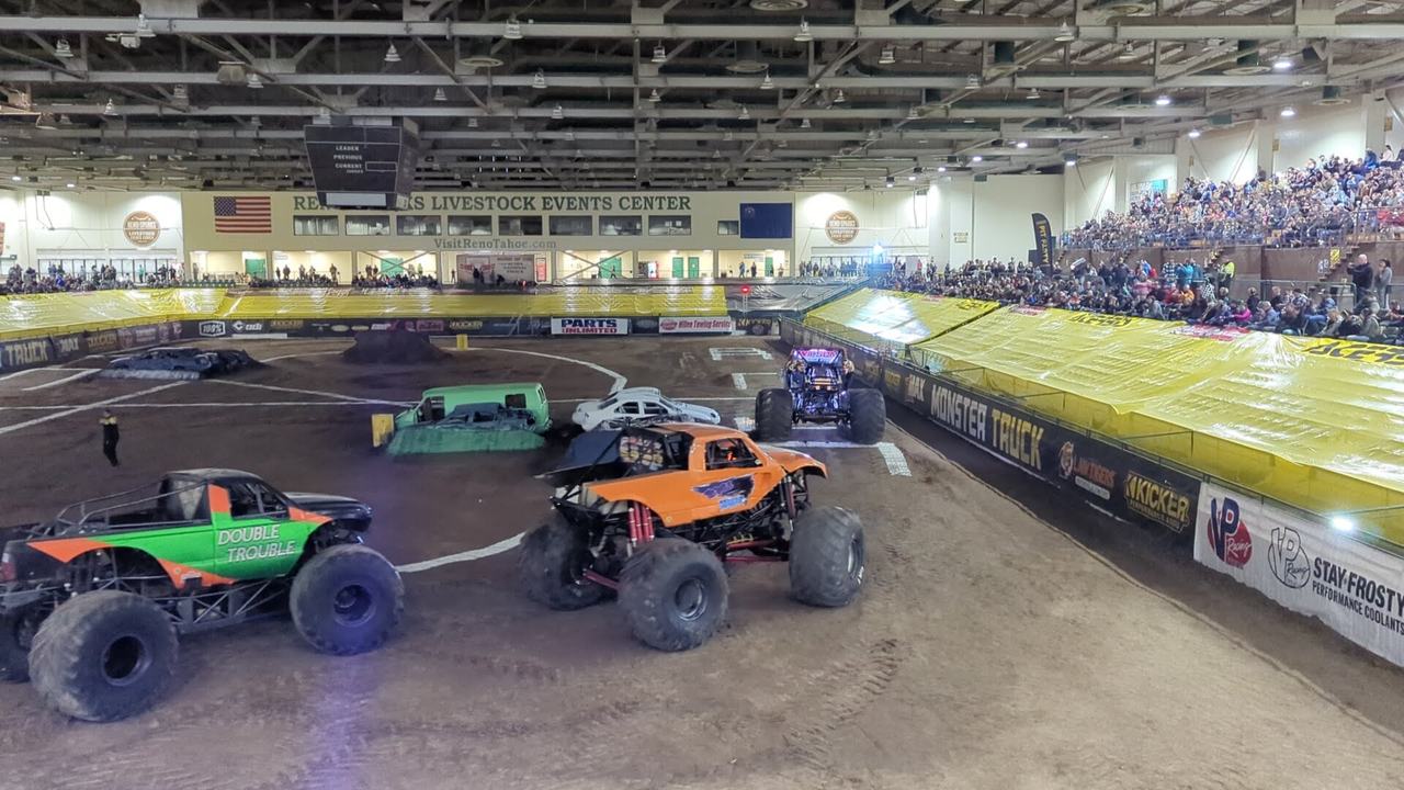 Monster trucks on the dirt track in front of packed stands at the KICKER Monster Truck Show, Reno Livestock Events Center