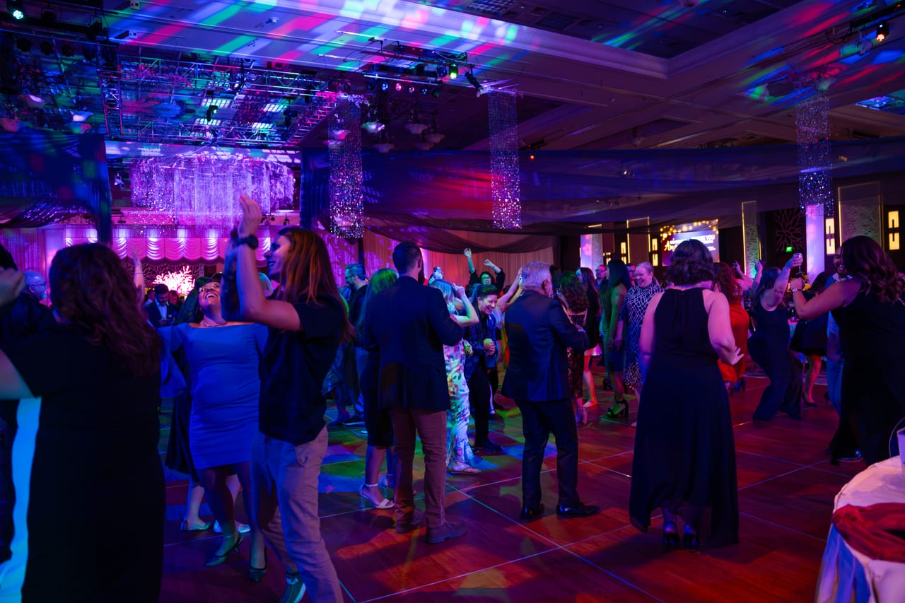 A packed dance floor under colored party lights in the Tuscany Ballroom