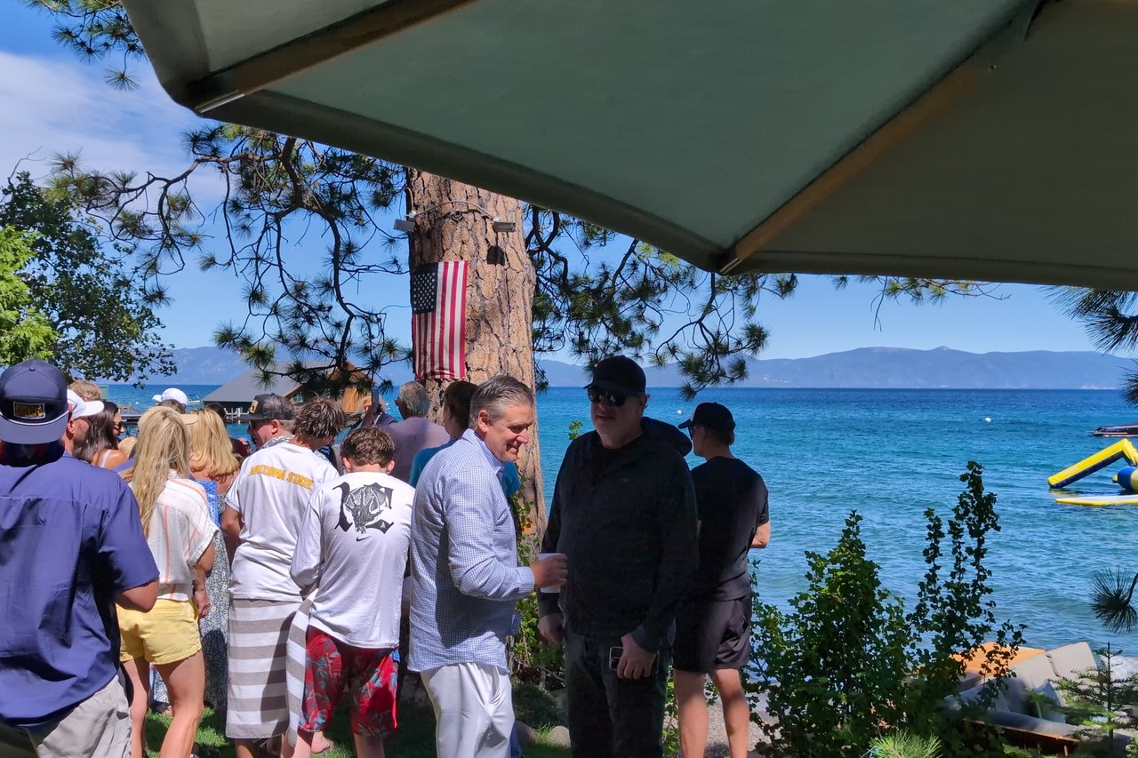 Guests in red, white and blue on the lawn by Lake Tahoe, a flag on the pine behind them