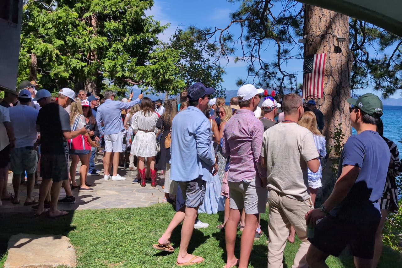 A packed lawn of Fourth of July guests between the pines and Lake Tahoe