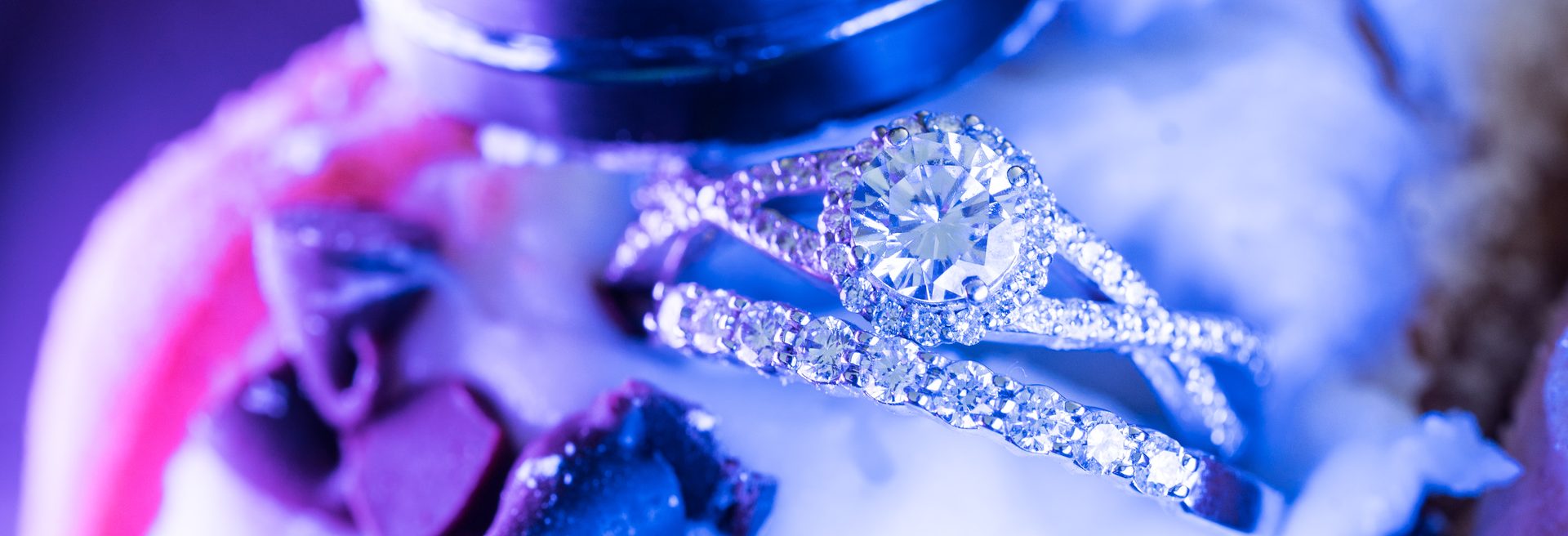 A black wedding band and a diamond engagement ring resting on an ice cream taco with chocolate chips under purple light
