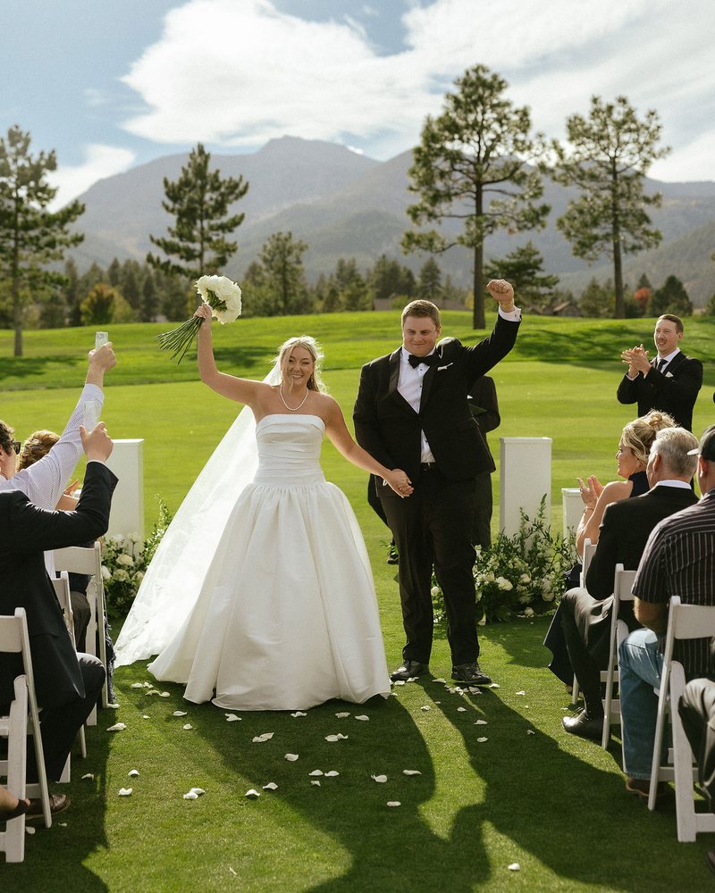 Ally raises her bouquet and Drew pumps his fist as they walk back up the aisle at Montreux Golf and Country Club