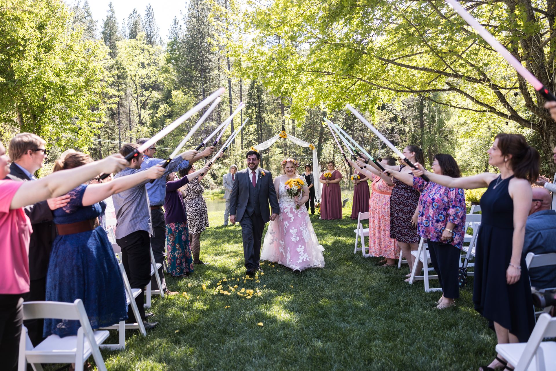 Abney and Chris walk back up the aisle under an arch of lightsabers held by their guests at Silverthorn Meadows