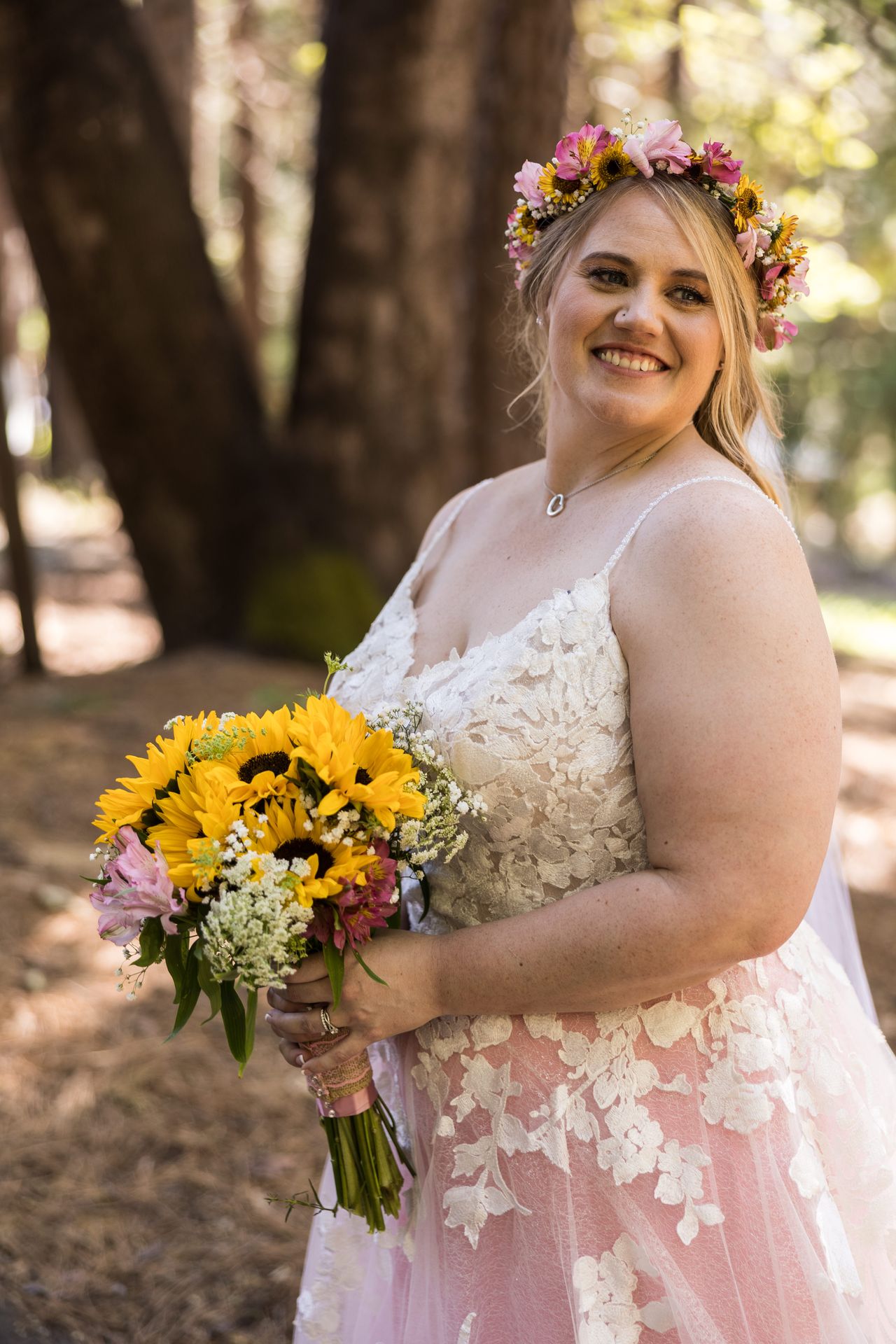 Abney smiles at the camera, holding her sunflower bouquet beside a pine tree