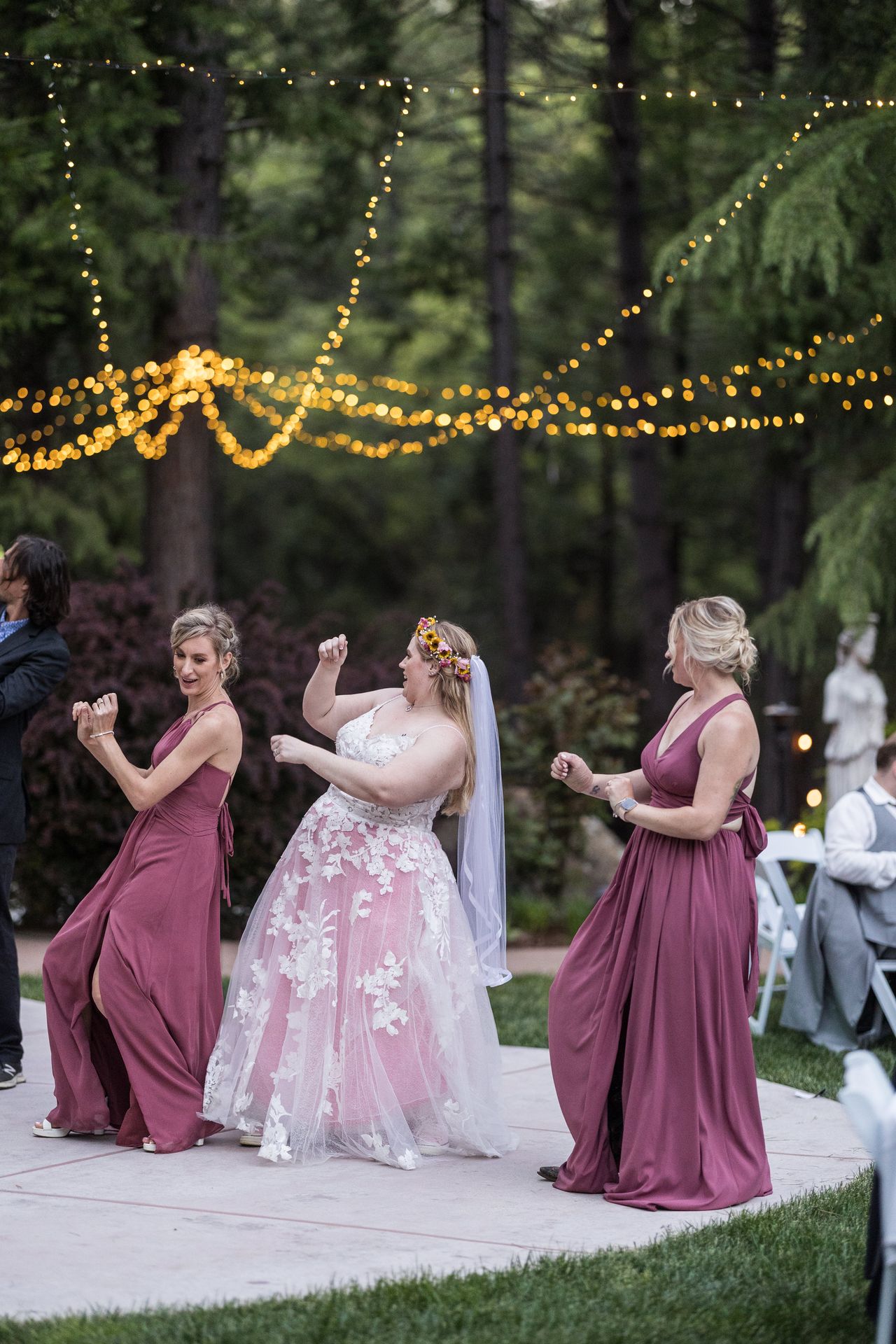 Abney dances with two of her bridesmaids beneath strands of string lights
