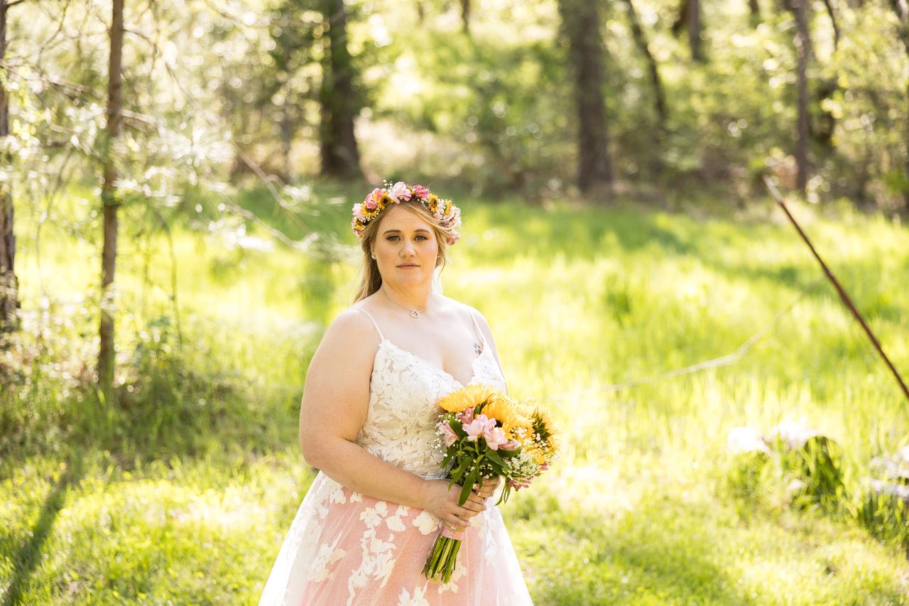 Abney looks straight at the camera in a sunlit meadow, holding her bouquet
