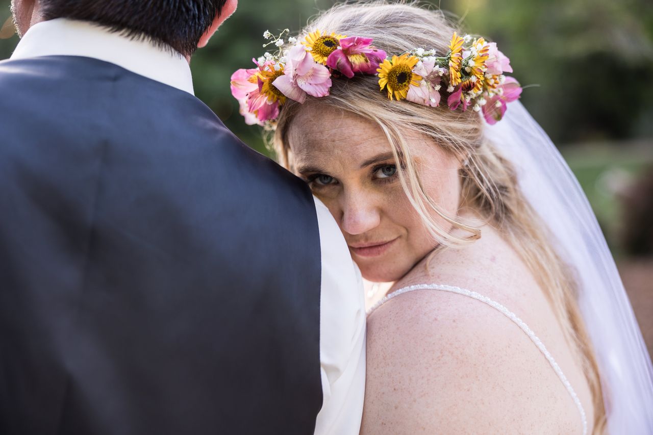 Abney glances at the camera over Chris's shoulder, her flower crown bright against the trees