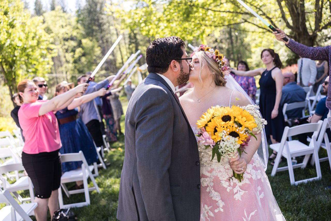 Abney and Chris stop for a kiss in the aisle as guests hold lightsabers over them
