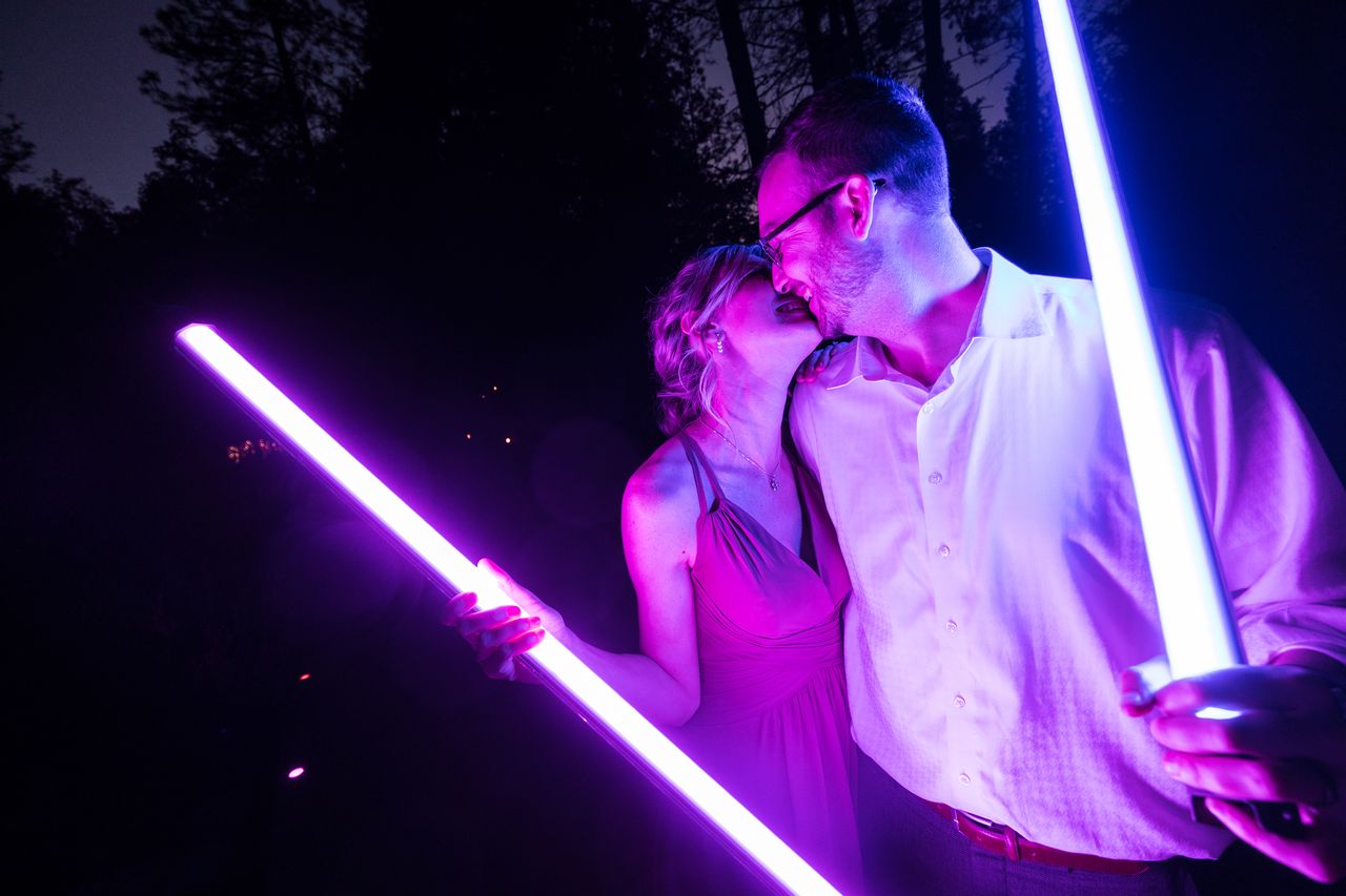 Two guests kiss in the dark, lit by the purple and blue lightsabers in their hands