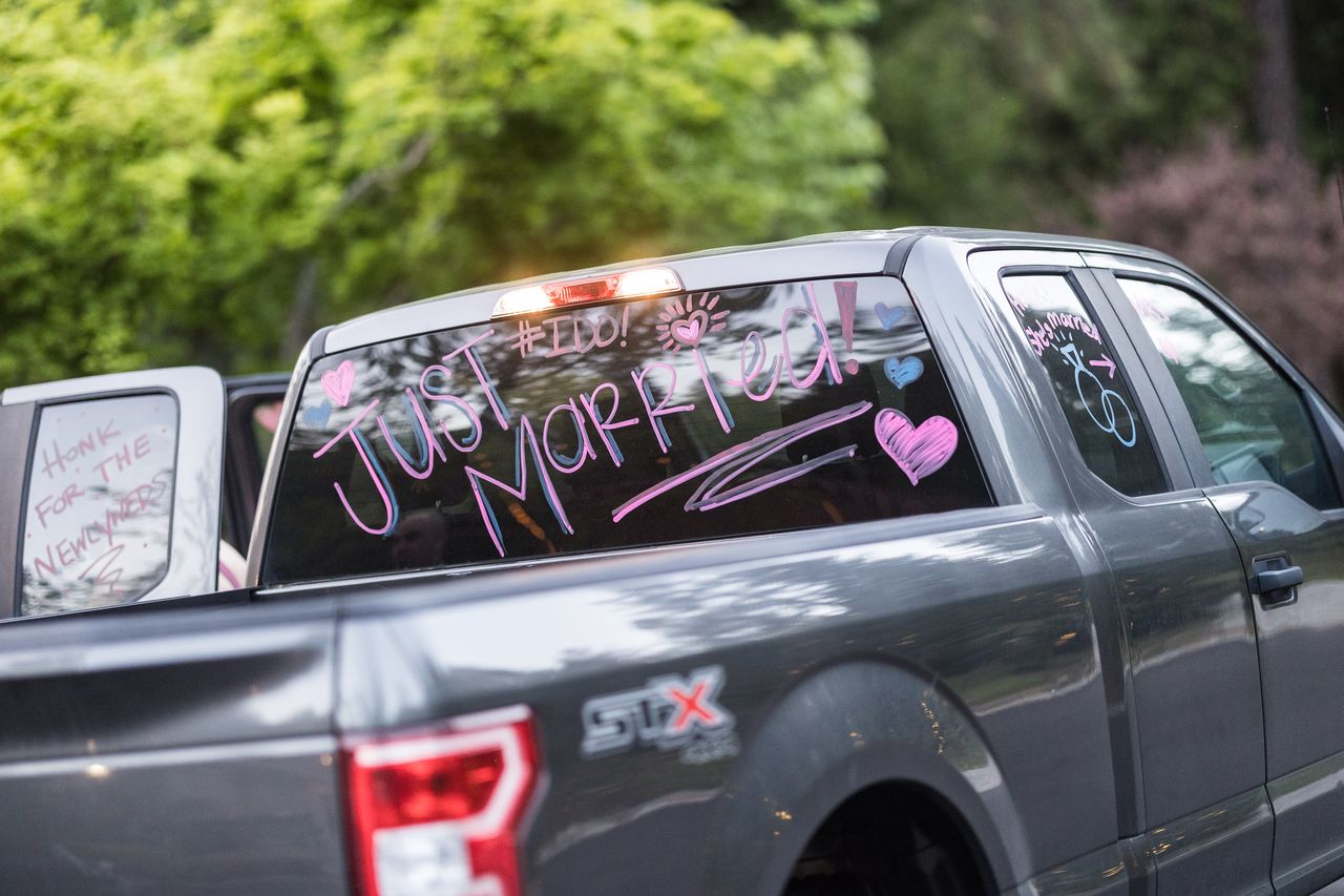 Just Married written in pink and purple across the back window of a pickup truck