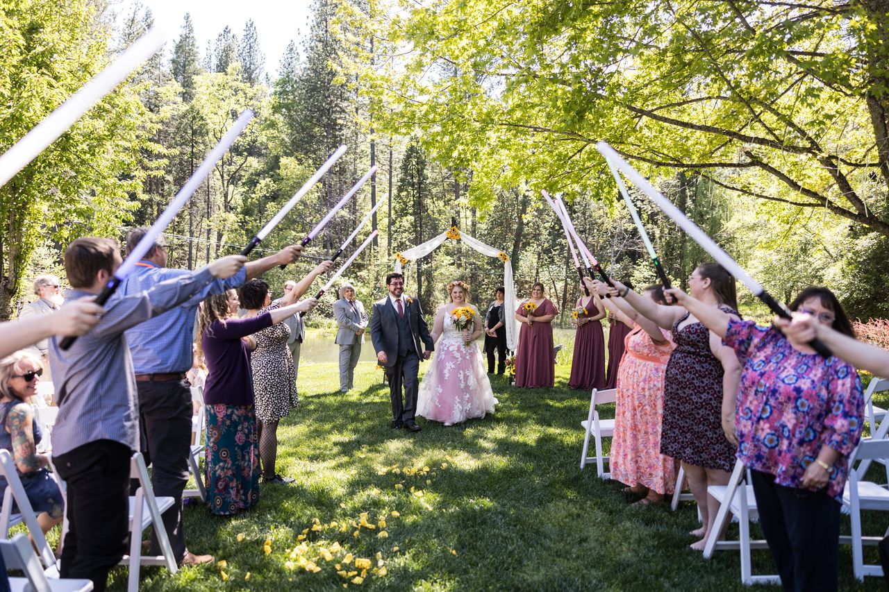 Guests on both sides of the aisle raise lightsabers into an arch for Abney and Chris