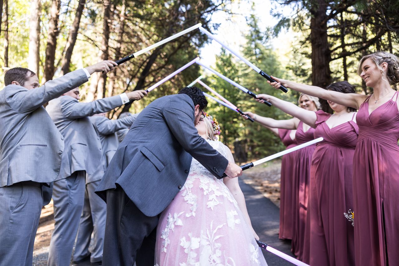 Chris dips Abney for a kiss while the wedding party crosses lightsabers above them