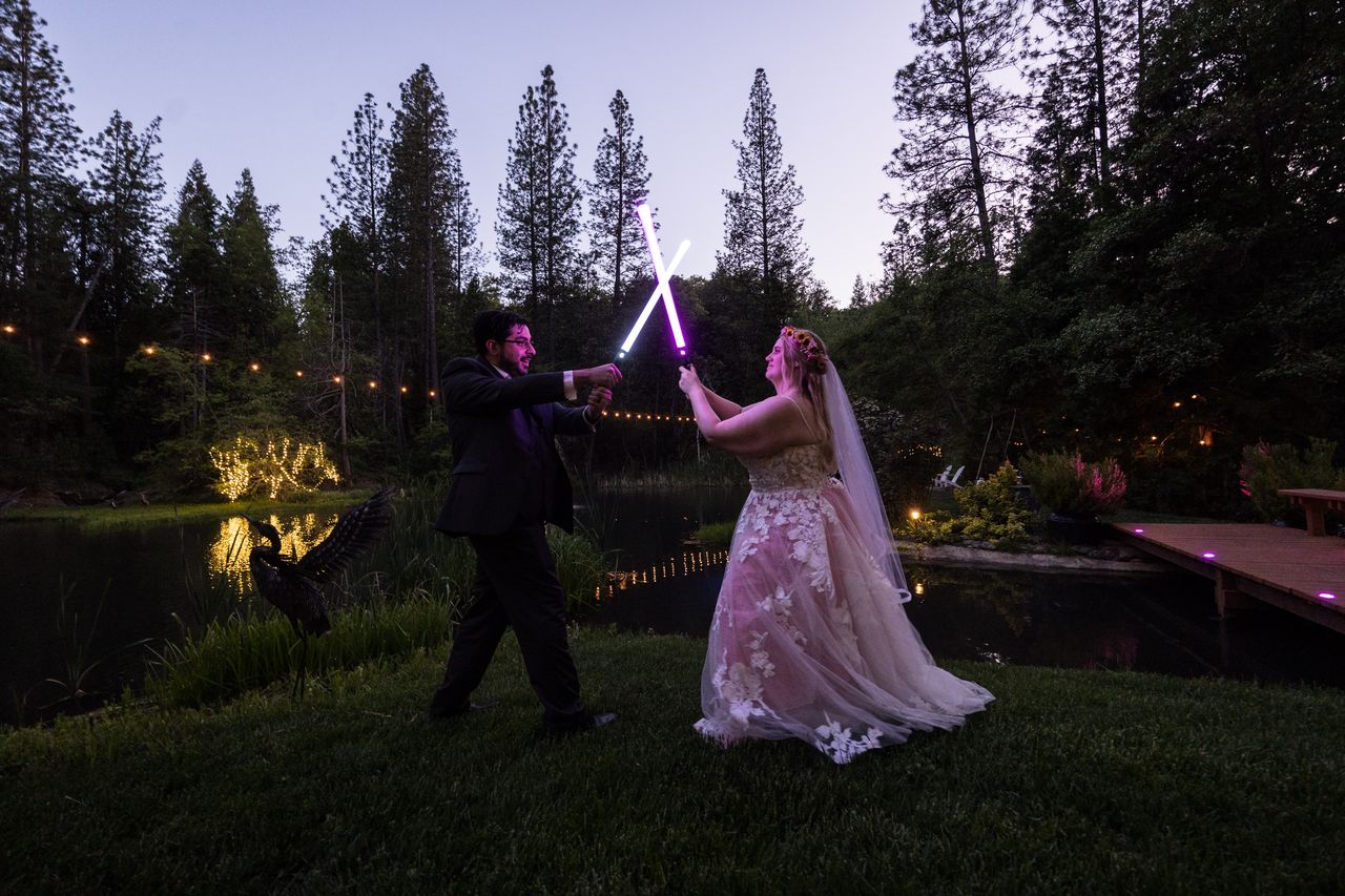 Abney and Chris cross their lightsabers into an X beside the pond at dusk