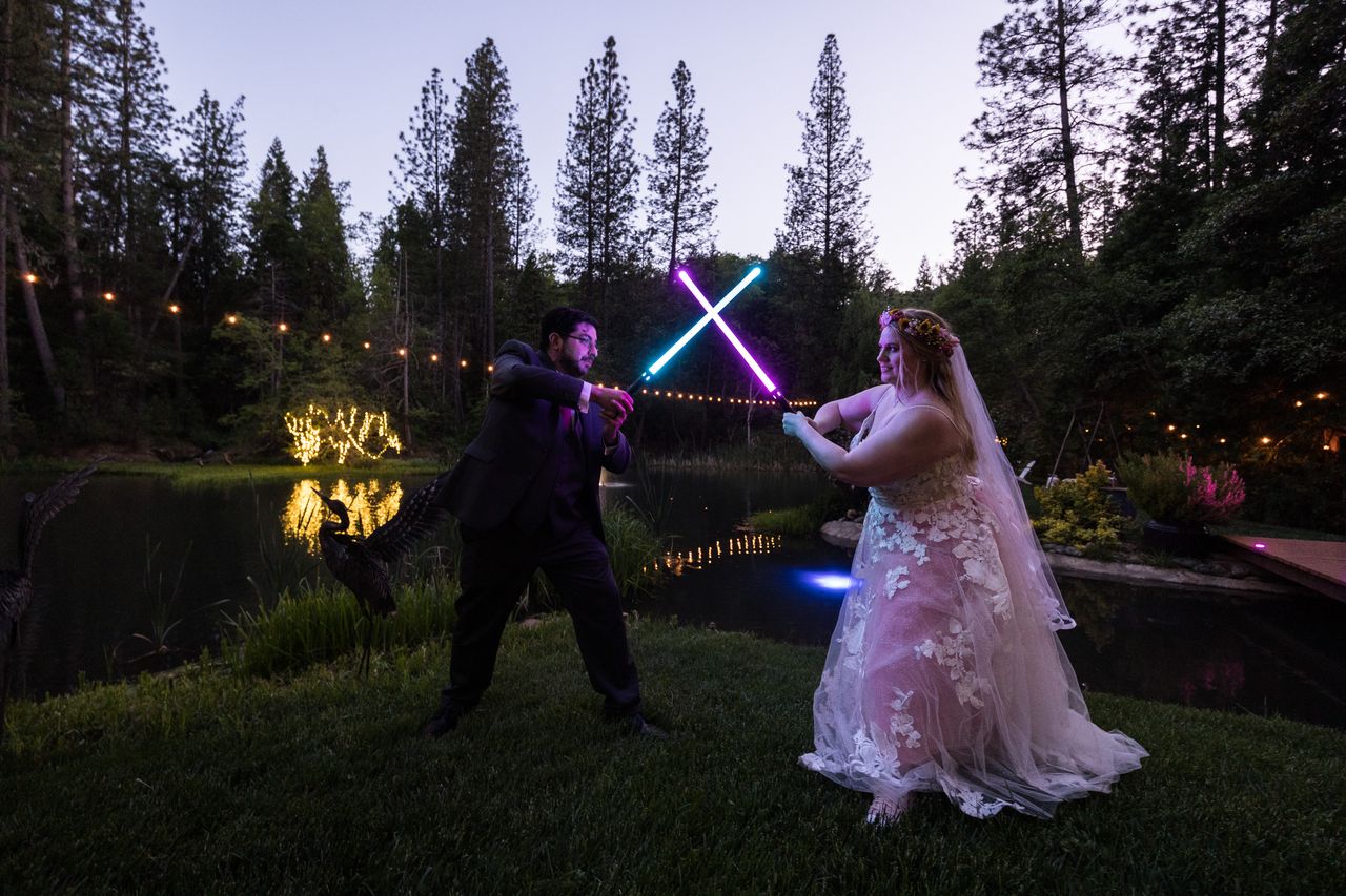 Abney and Chris cross glowing lightsabers beside the pond at dusk
