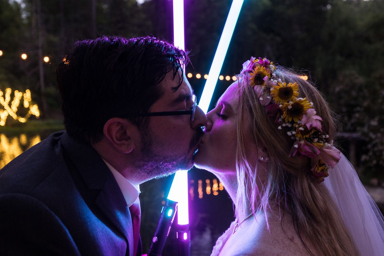 Abney and Chris kiss with two lightsabers glowing behind them
