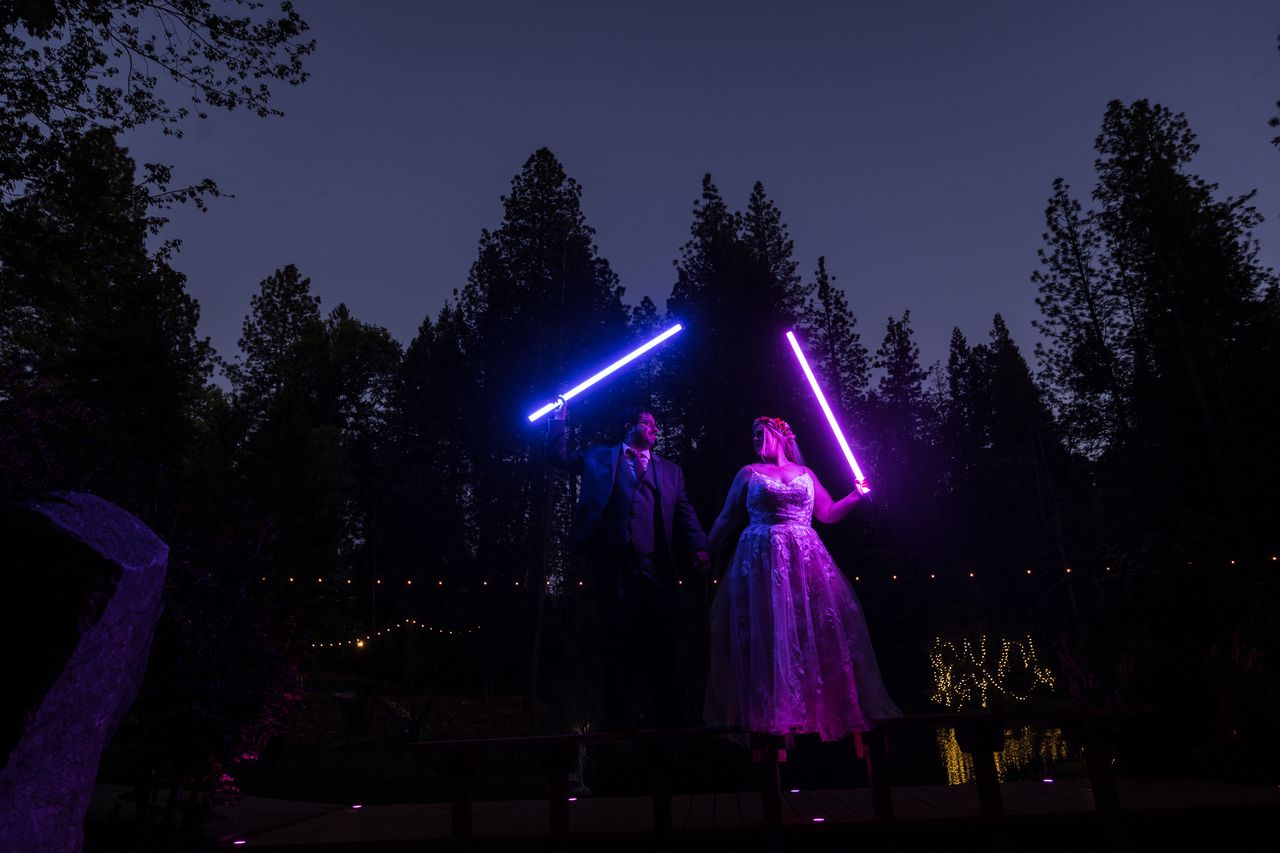 Abney and Chris raise a blue lightsaber and a purple one against the night sky
