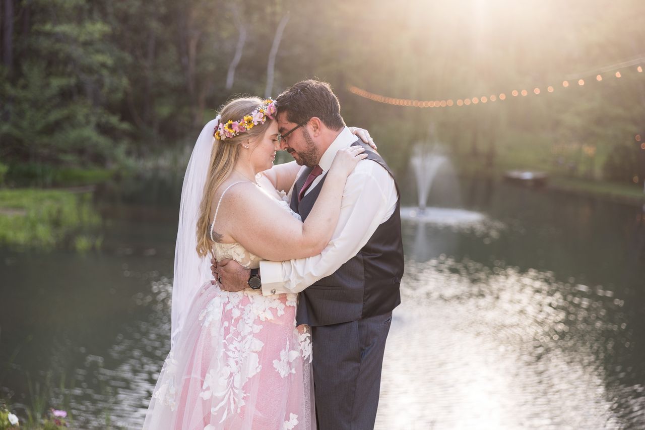 Abney and Chris stand forehead to forehead beside the pond in the golden evening light