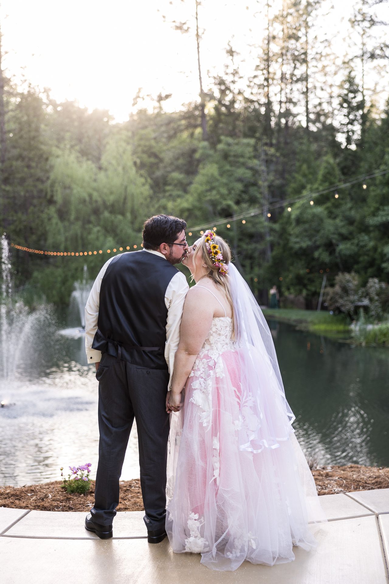 Abney and Chris kiss on the patio at the edge of the pond, under a strand of string lights