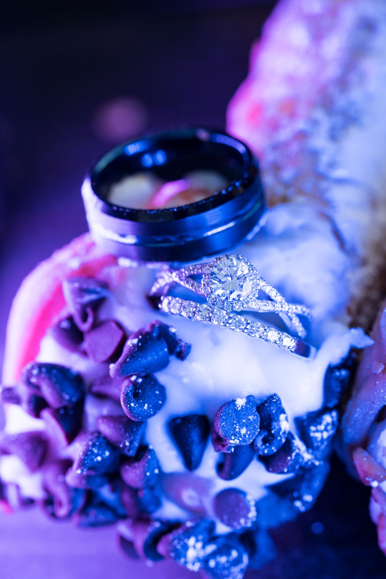 The wedding rings sit on a cannoli dipped in chocolate chips, lit in blue and purple