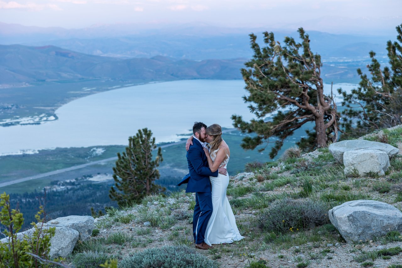Ali and Robert kiss on the ridge beside a windswept pine above Washoe Lake