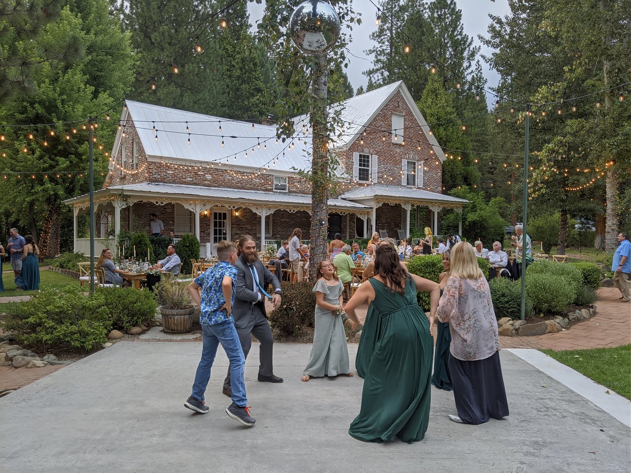 Bridesmaids in green dance with guests in front of the brick house at Twenty Mile House