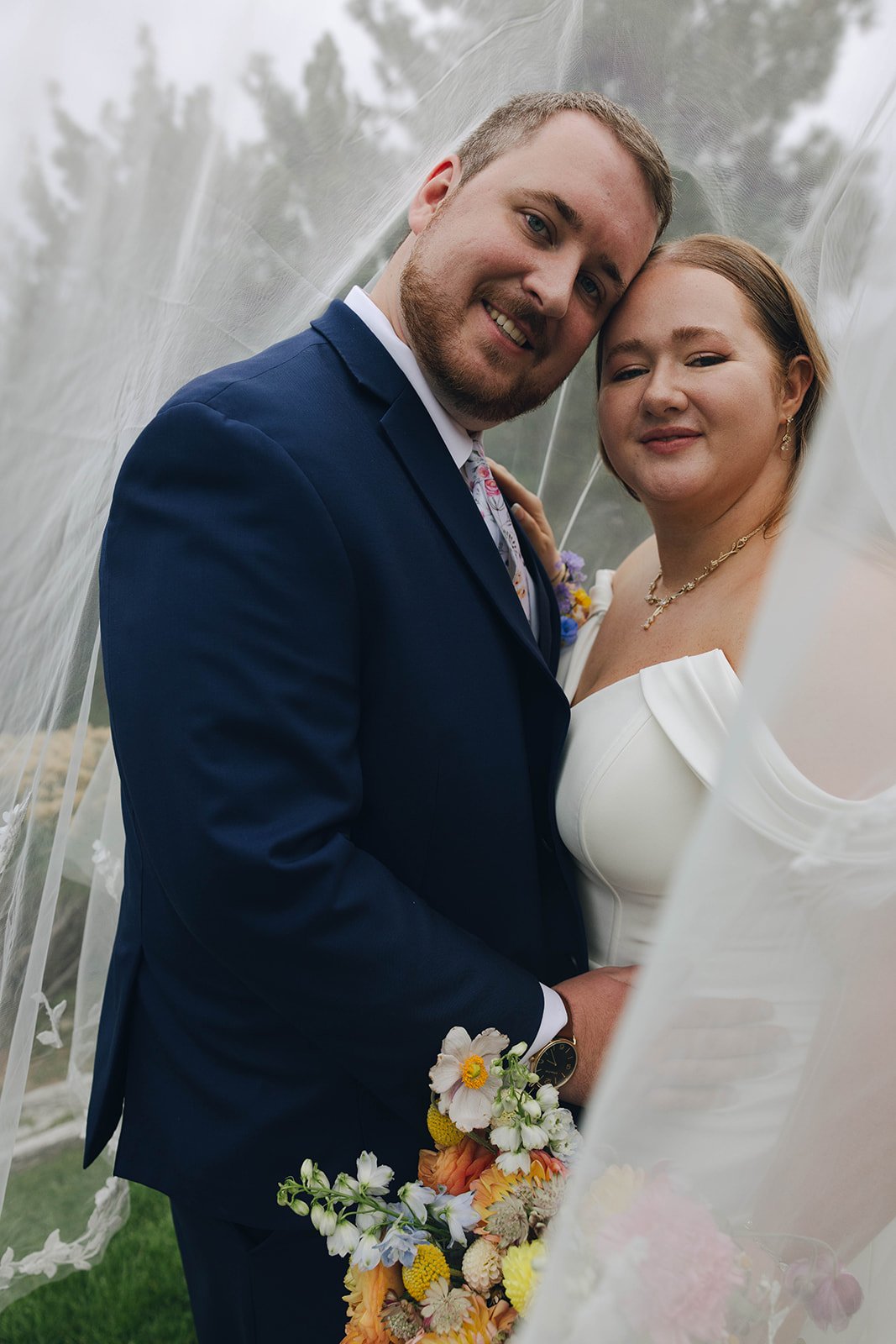 Autumn and Peter stand cheek to cheek as her veil blows across the frame