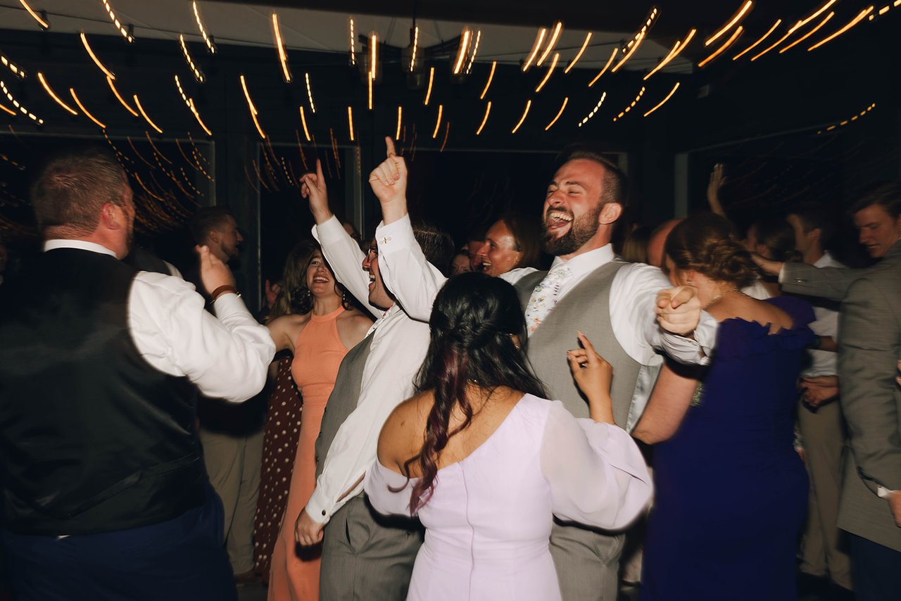 Groomsmen laugh with their hands up on the dance floor