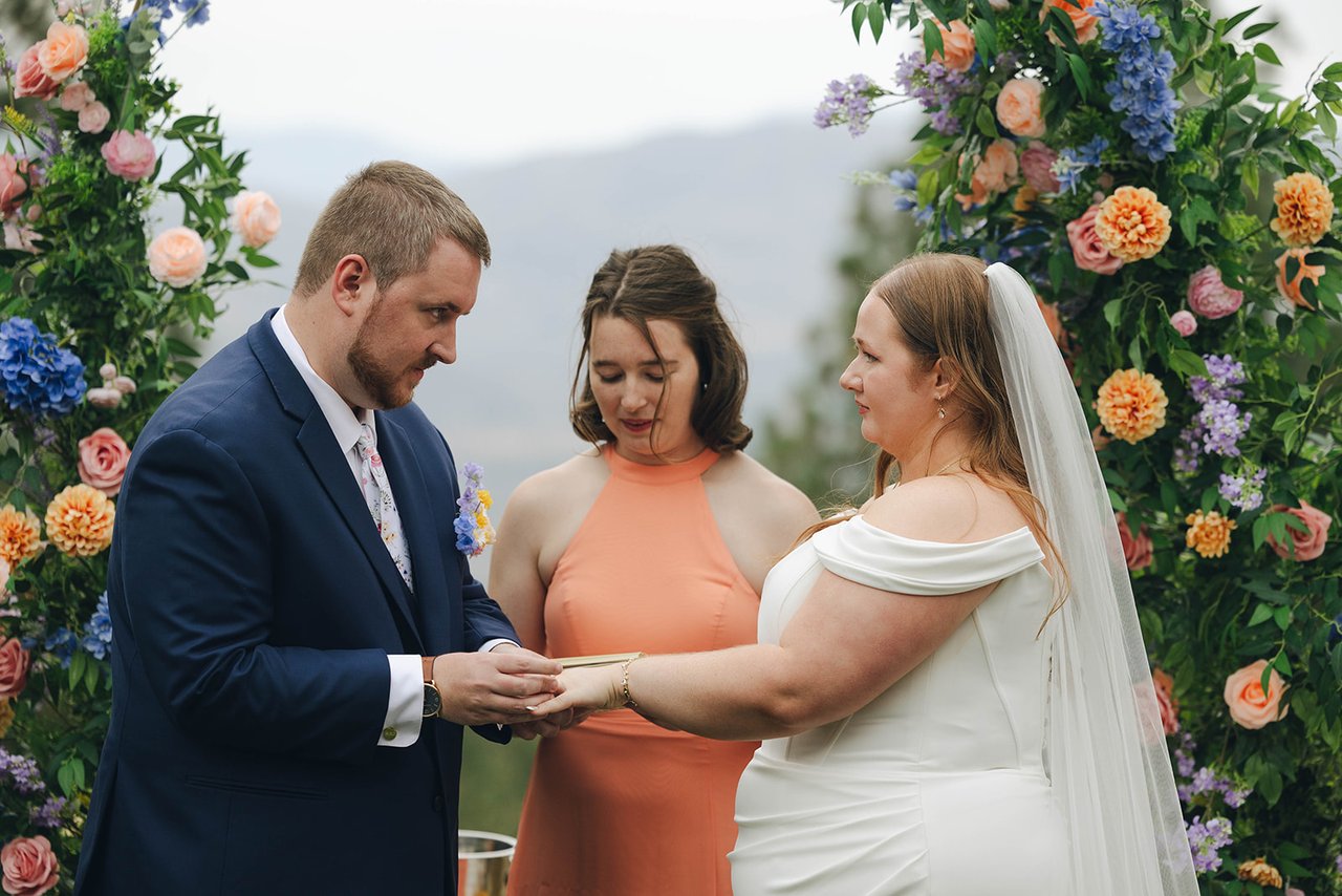 Peter slides the ring onto Autumn's finger at the floral arch