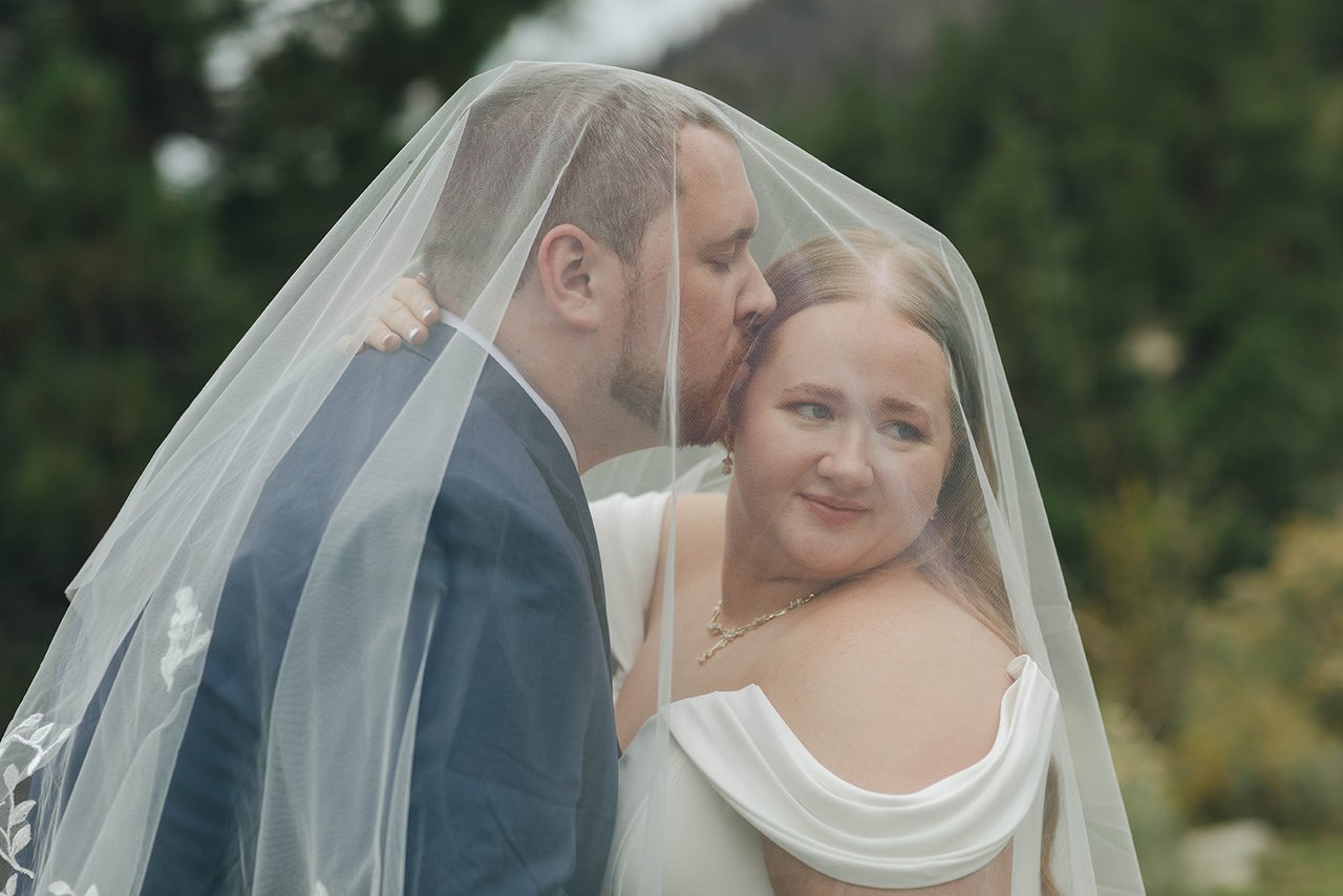 Peter kisses Autumn's cheek under her veil while she looks toward the camera