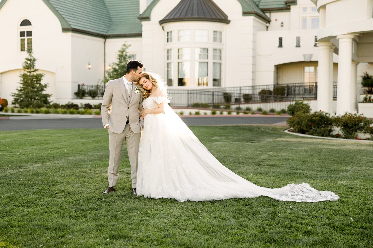 Chris kisses Britt on the forehead as her long train spreads across the lawn in front of the clubhouse
