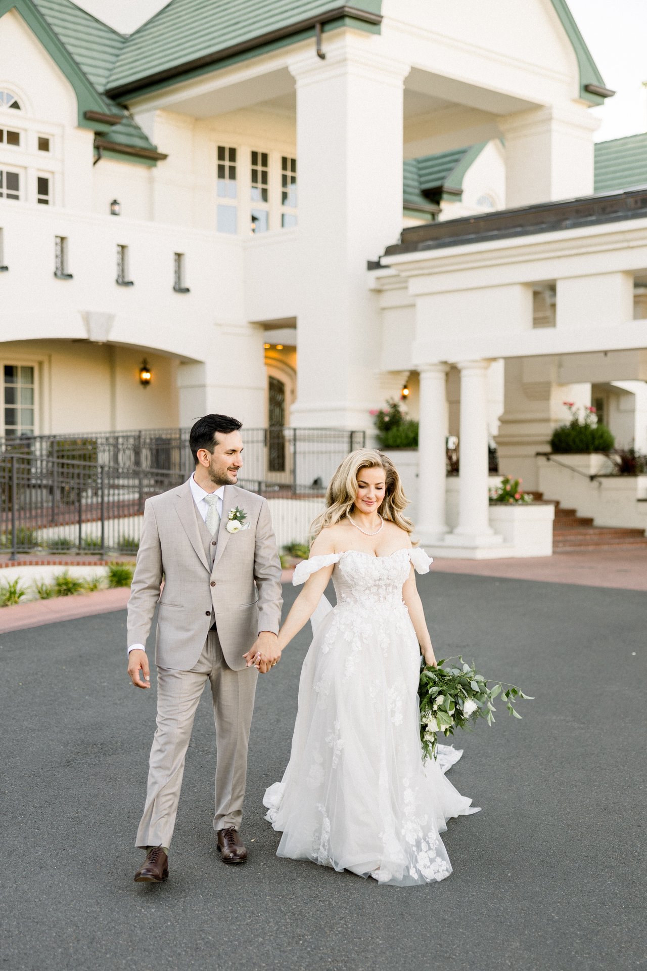 Britt and Chris walk hand in hand in front of the clubhouse