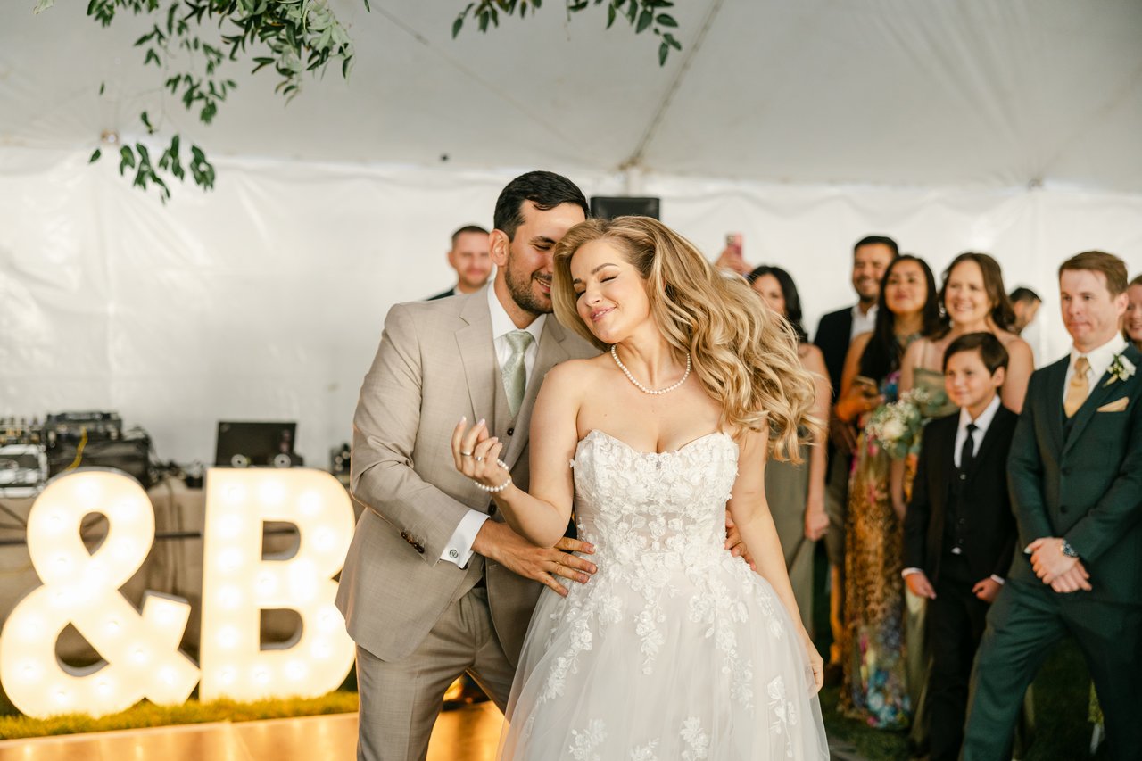 Britt leans into Chris by the glowing marquee letters as their wedding party smiles behind them