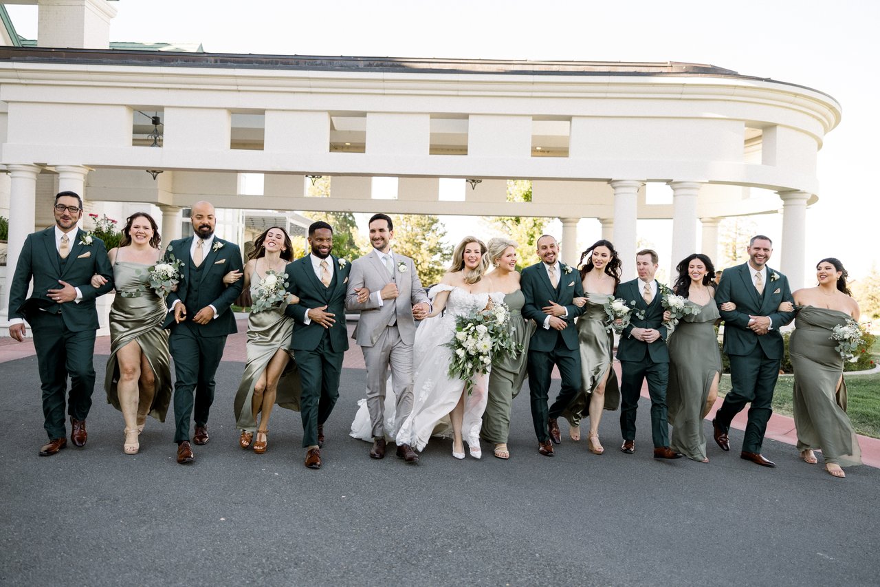 The wedding party walks arm in arm across the drive