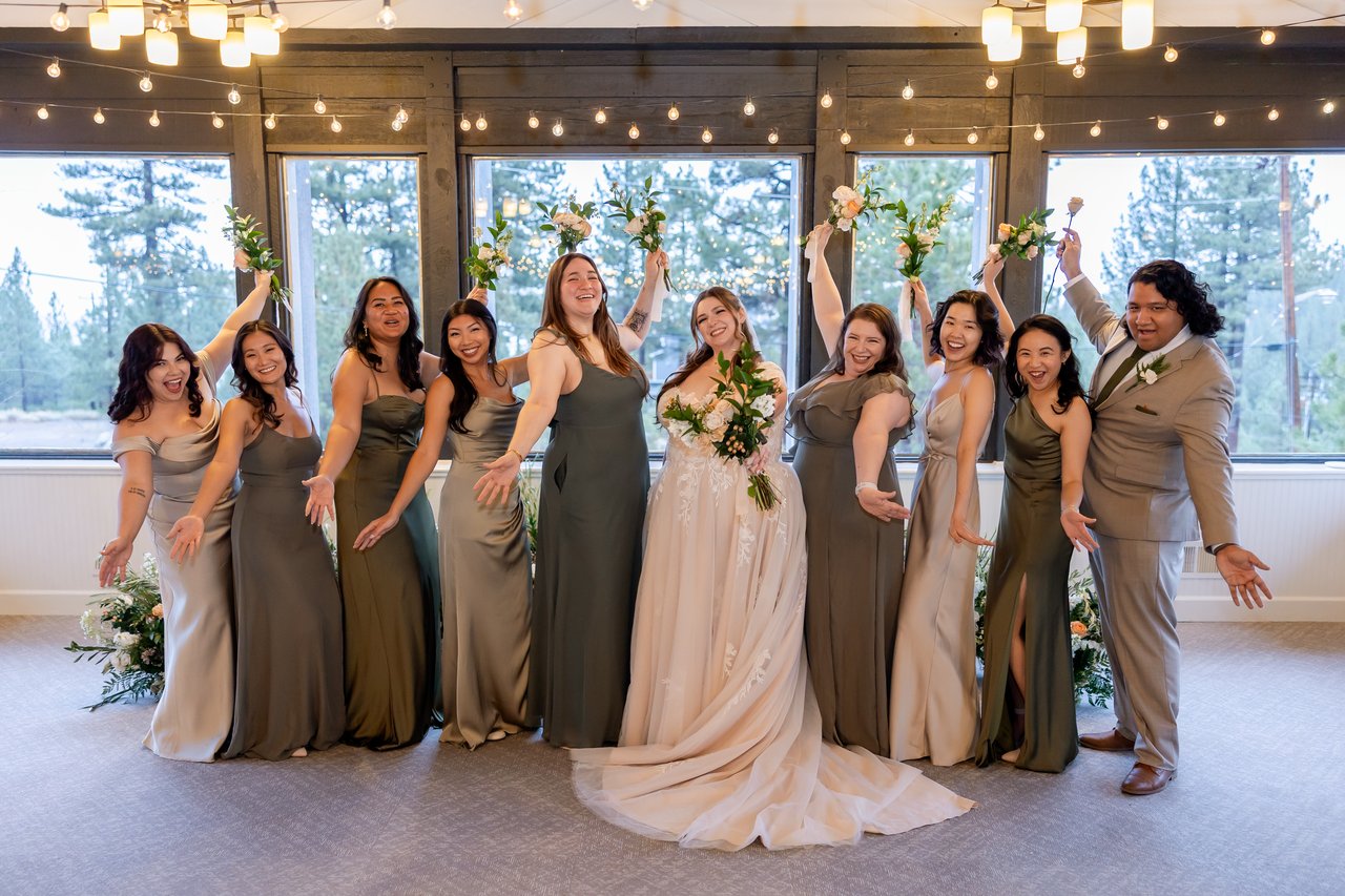 The wedding party cheers with their bouquets raised by the windows