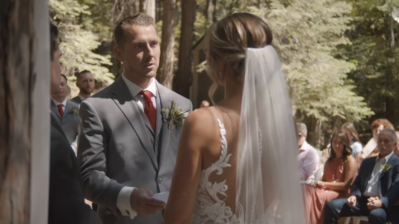 Scott reads his vows to Danielle at the arch as guests watch from the forest seats