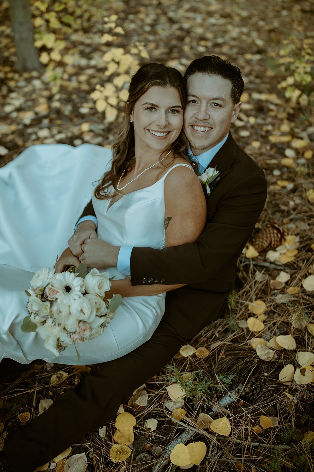 Emily and Devin sit together in the golden aspen leaves, both smiling