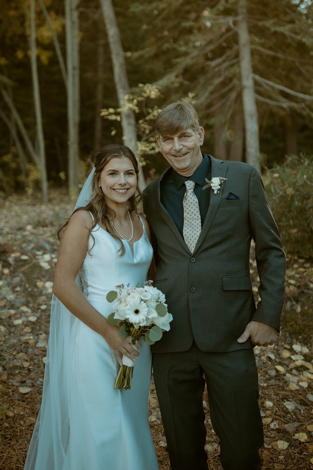 Emily smiles with a man in a gray suit in the forest