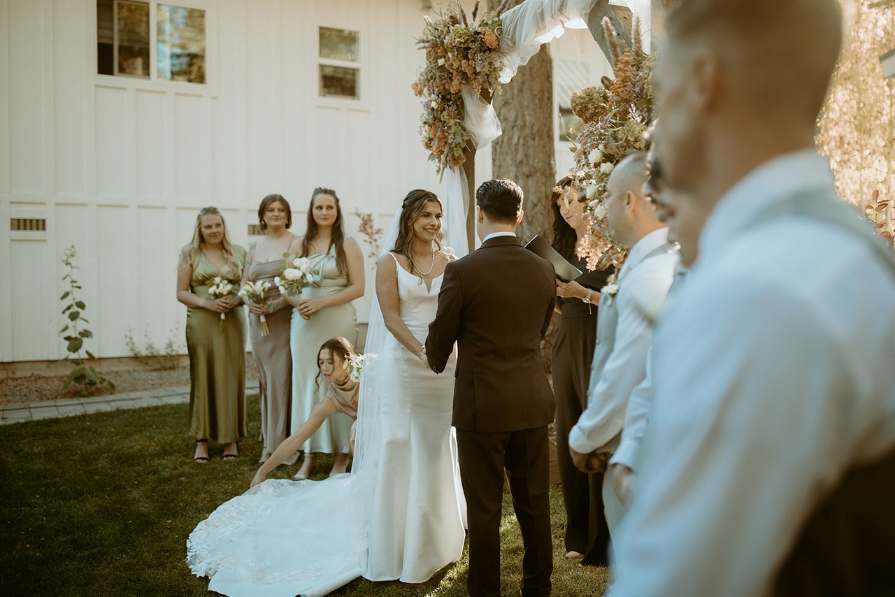 A bridesmaid fixes Emily's train at the arch
