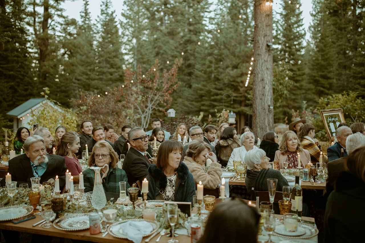 Guests at the long candlelit tables at dinner, pines behind