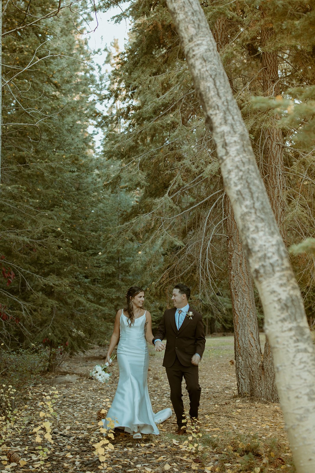 Emily and Devin walk hand in hand through the trees