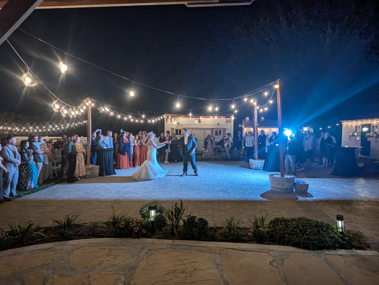 Emily and Logan begin their first dance in blue light as their guests circle the patio