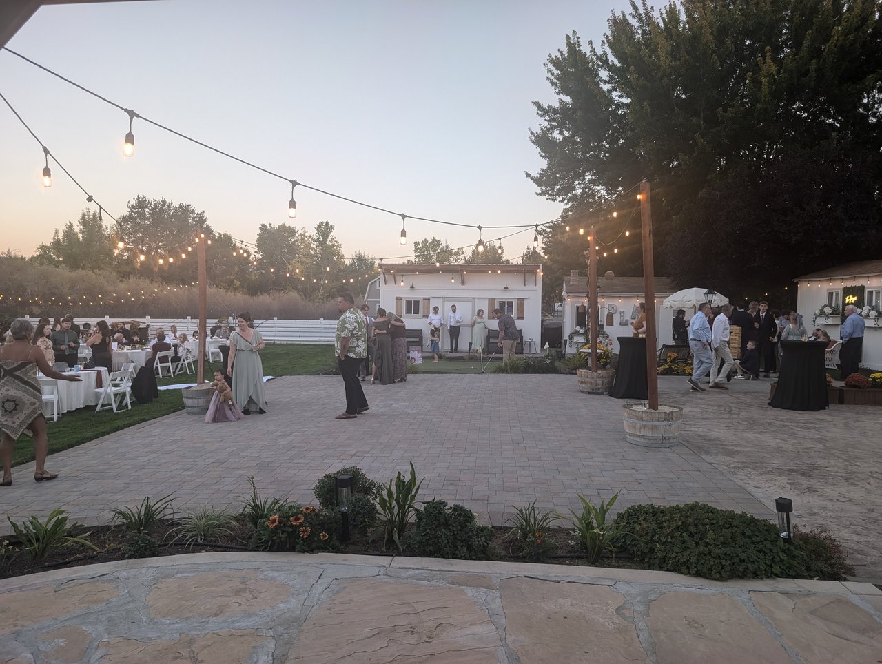 String lights over the patio dance floor at dusk as guests gather by the white cottages