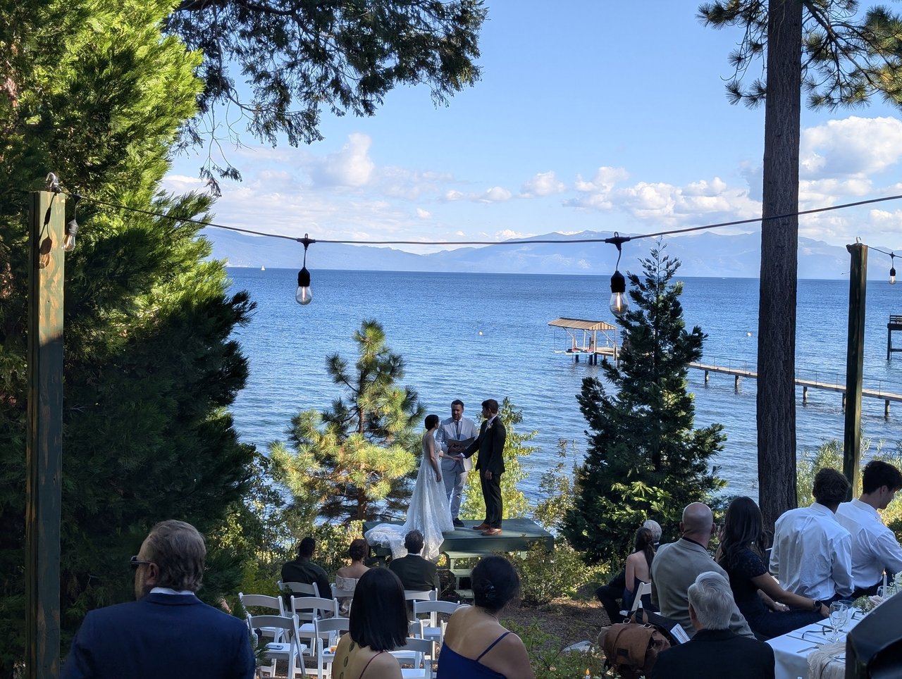 Guests watch Emma and Jackson's ceremony at the edge of the lake under string lights