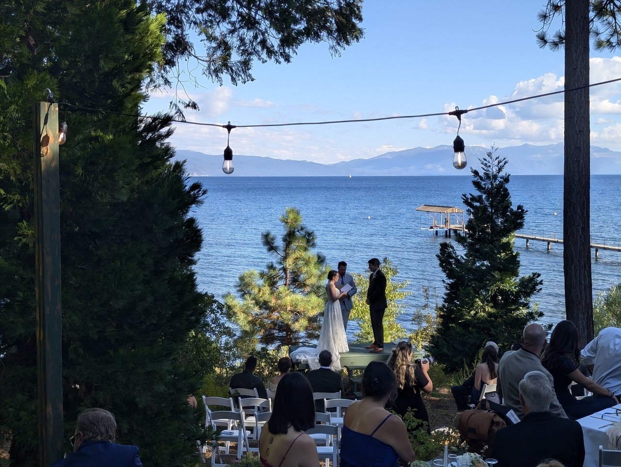 Emma and Jackson face each other during their vows, framed by pines with Lake Tahoe behind them